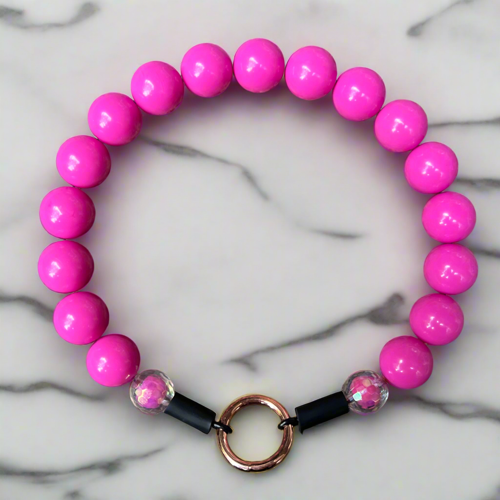 Pink beaded bracelet with a black and copper clasp on a marble background