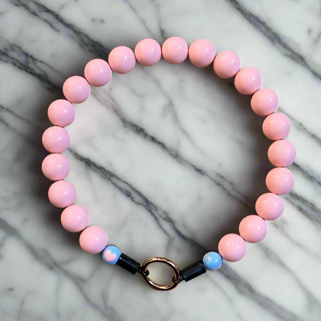 Pink beaded bracelet with a black and gold clasp on a marble surface
