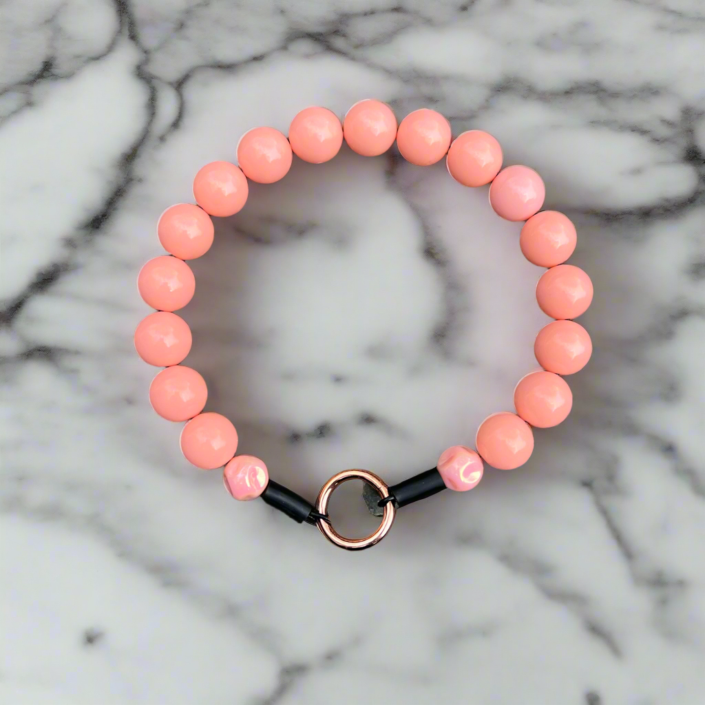 Peach-colored beaded bracelet with a black and gold clasp on a marble background