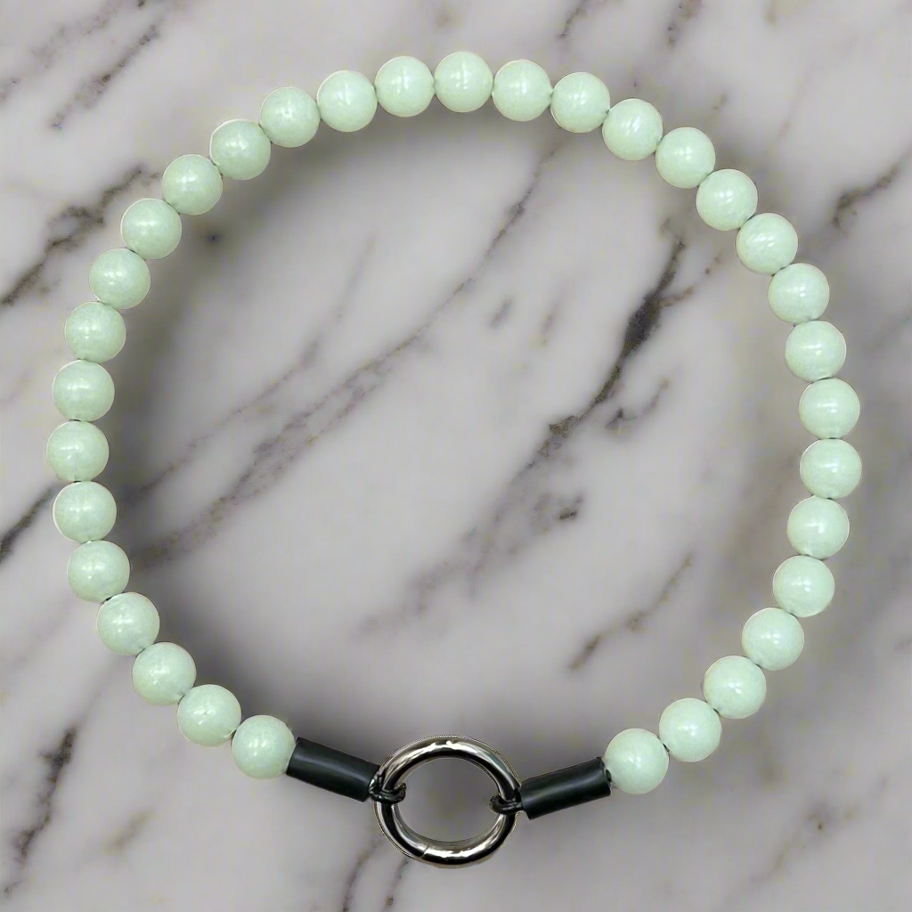 Light green beaded bracelet with a black band and silver clasp on a marble background