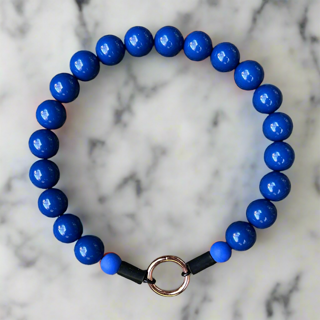 Blue beaded bracelet with a black band and gold clasp on a marble background