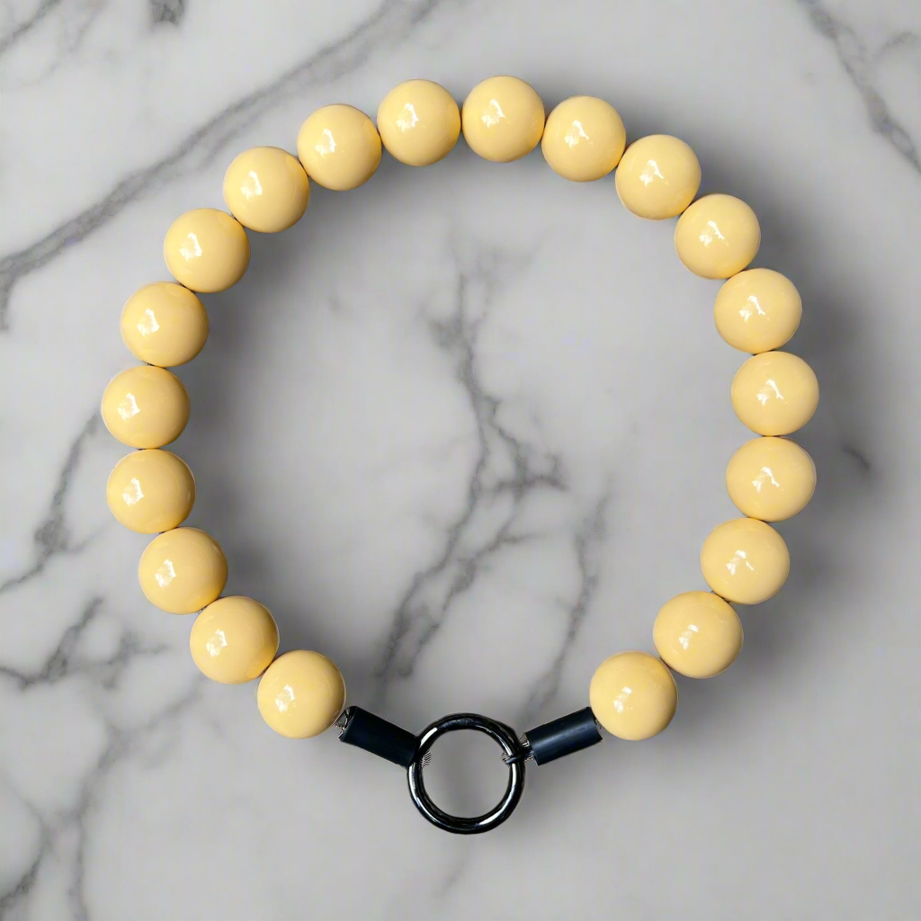 Yellow beaded bracelet with a black clasp on a marble background