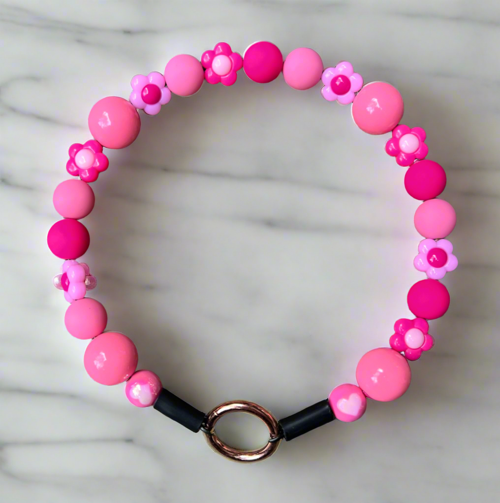 Pink beaded bracelet with a black band and gold clasp on a marble background