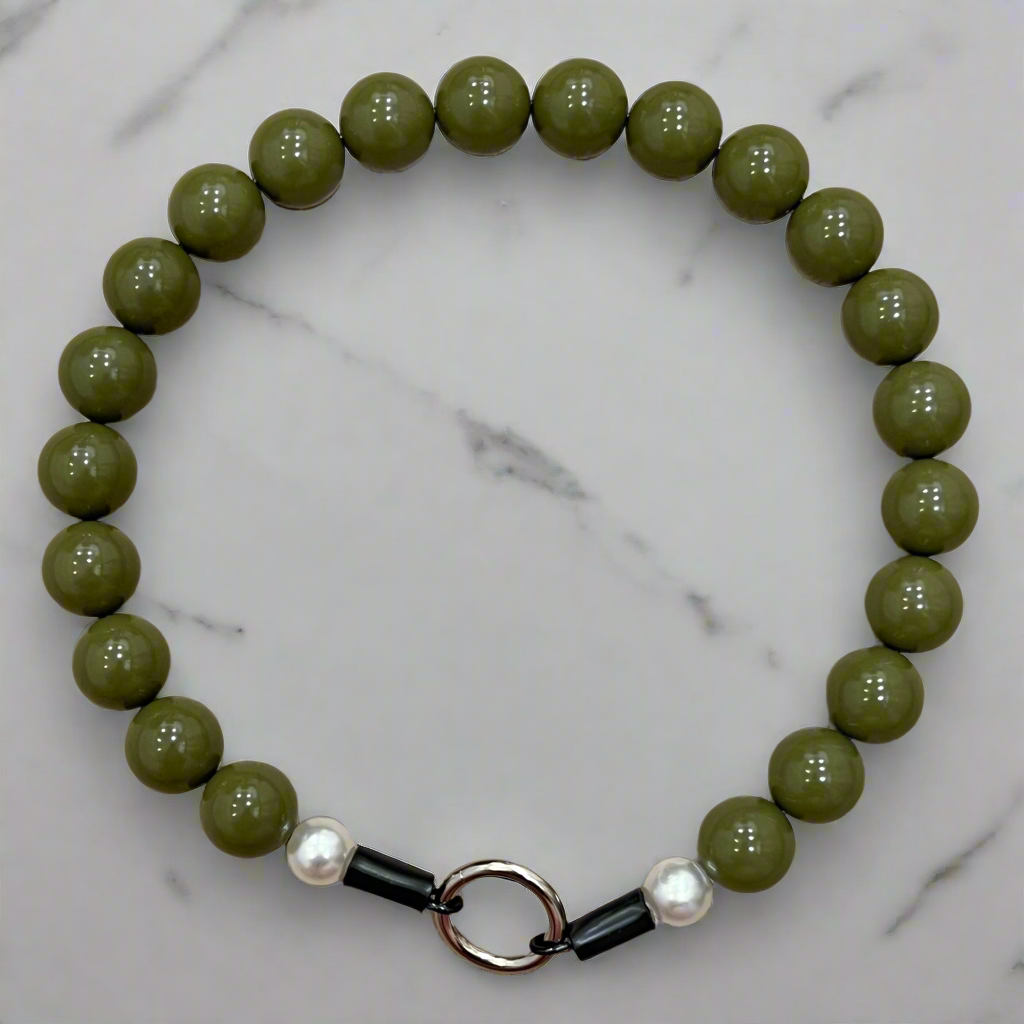 Green beaded bracelet with a black and silver clasp on a marble background