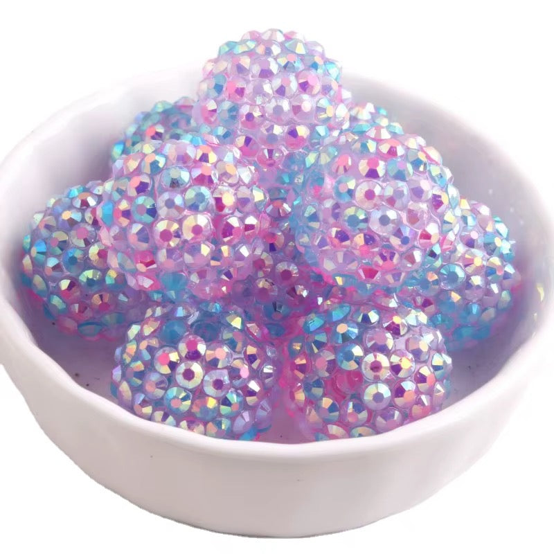 A pile of iridescent, faceted gel beads in pink, blue, and purple tones, displayed inside a small white ceramic bowl on a white background.