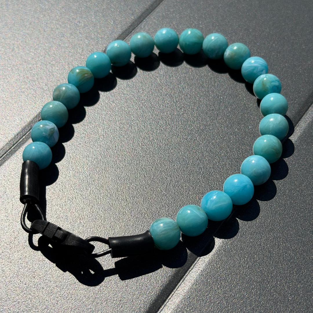 POPNCO Poseidon 12mm Beaded Pet Collar. teal Marble Acrylic and Resin beads on Aircraft Grade Stainless Steel Wire. Turquoise beaded pet collar with black clasp on a reflective surface