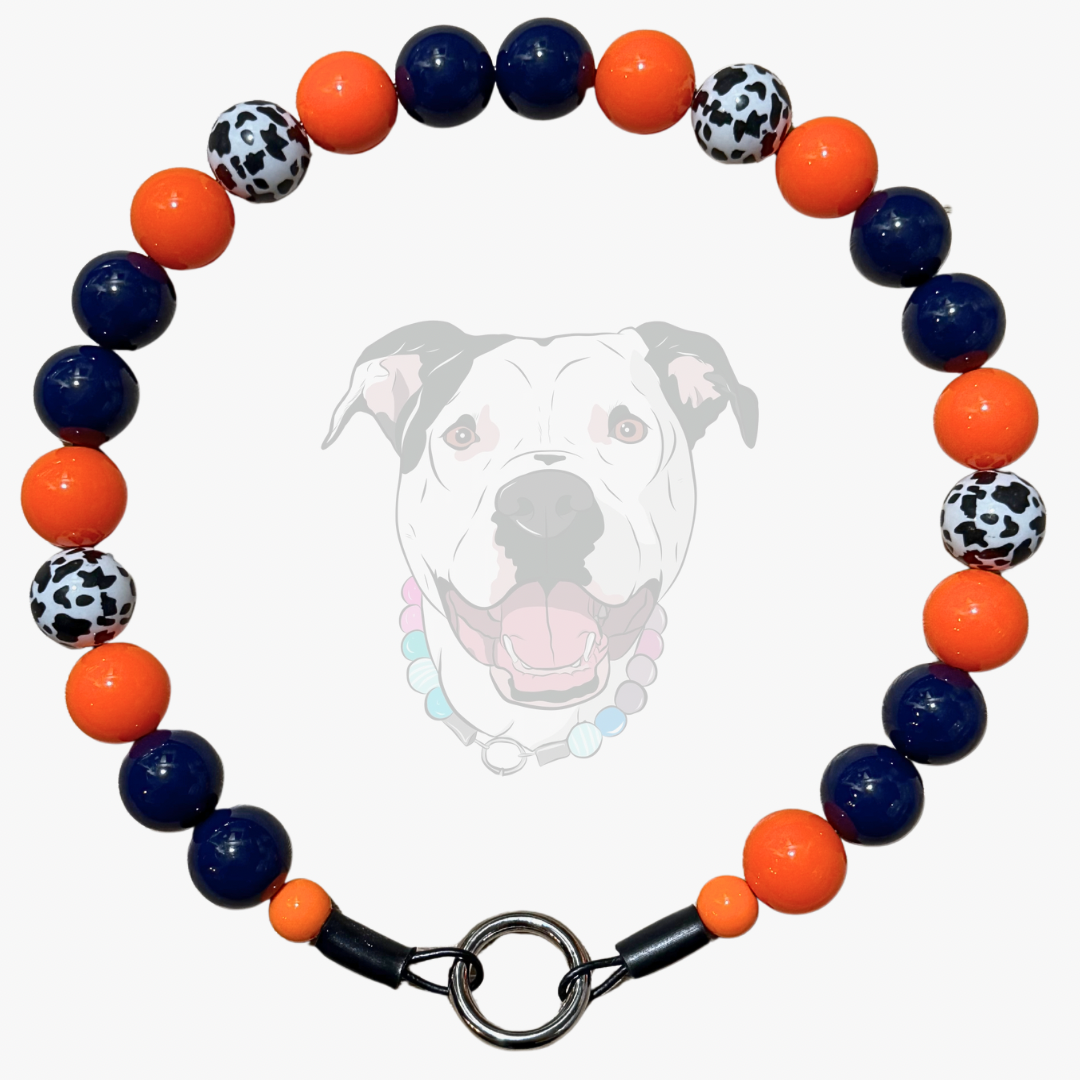 A beaded dog collar featuring alternating navy blue, bright orange, and black-and-white spotted beads, with a silver metal clasp. A faint graphic of a dog's face is visible in the background.