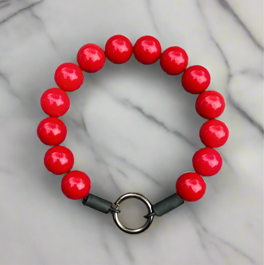 Red beaded bracelet with a gray strap on a marble background