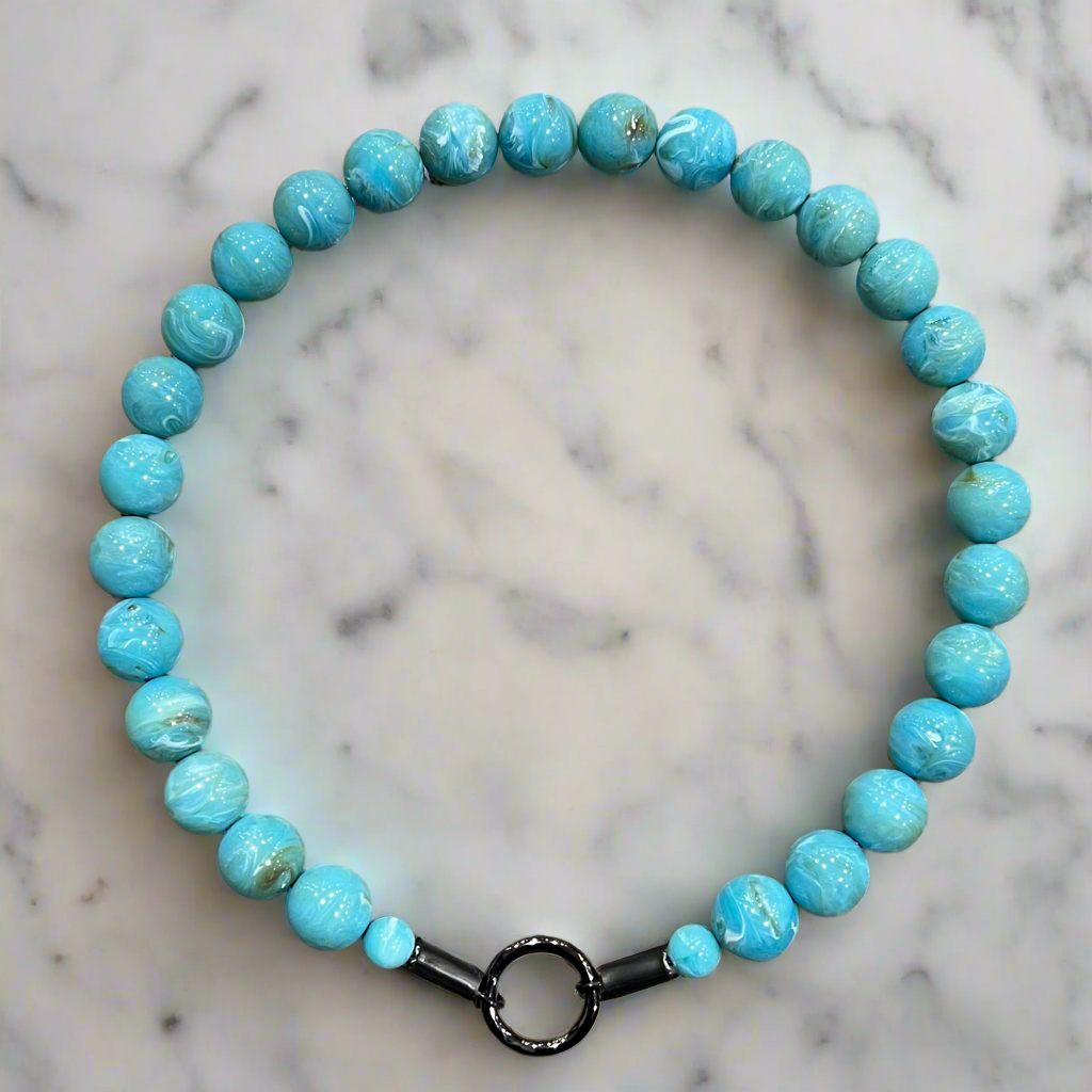 Turquoise beaded bracelet with a black clasp on a marble background