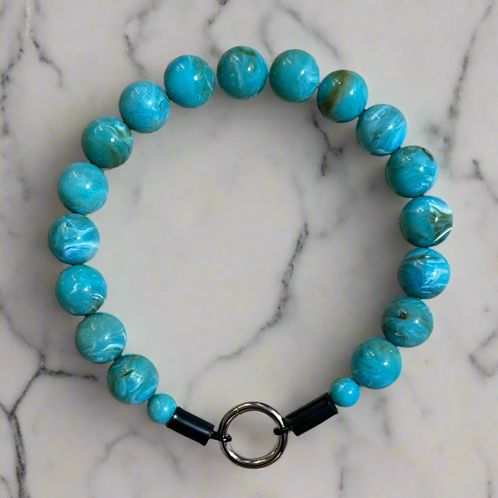 Turquoise beaded bracelet with a black strap on a marble background