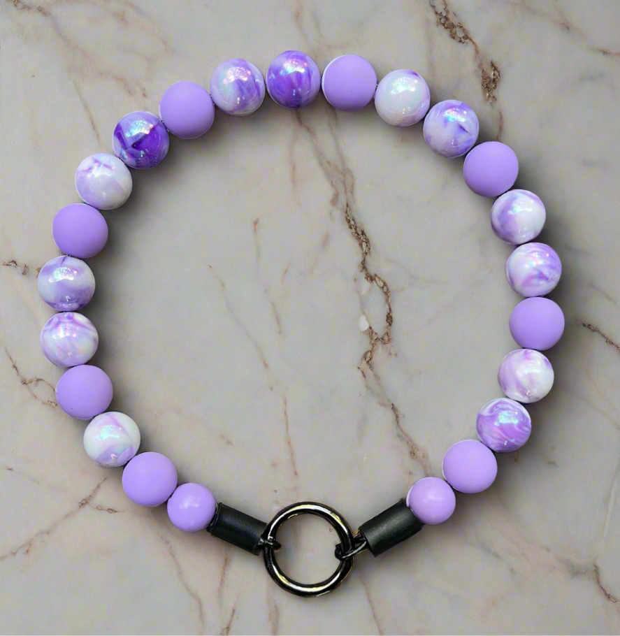 Purple and white beaded bracelet with a black clasp on a marble surface