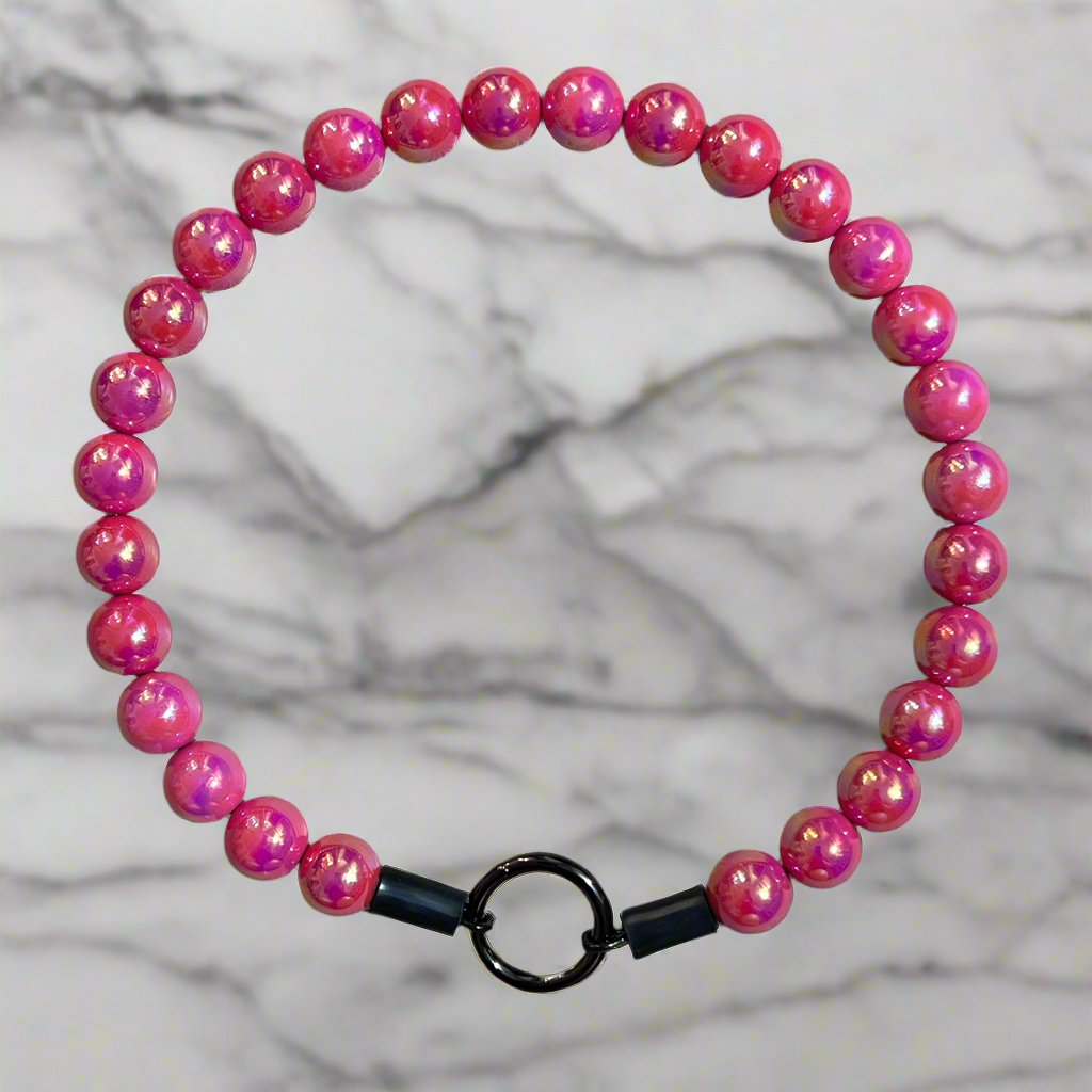 Pink beaded bracelet with a black clasp on a marble background