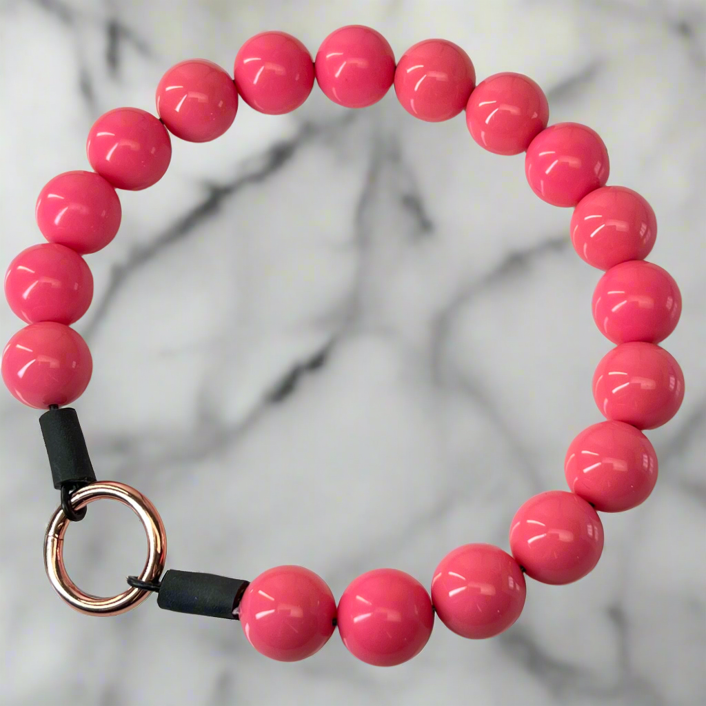 Pink beaded bracelet with a black and rose gold clasp on a marble background