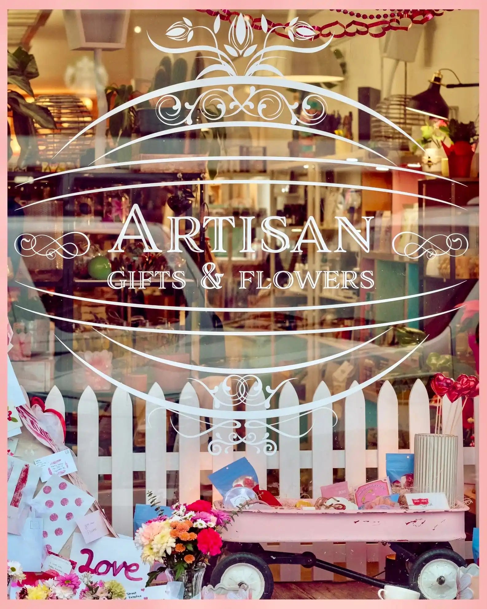 Storefront with 'Artisan Gifts & Flowers' sign, decorated with a white picket fence and floral arrangements.