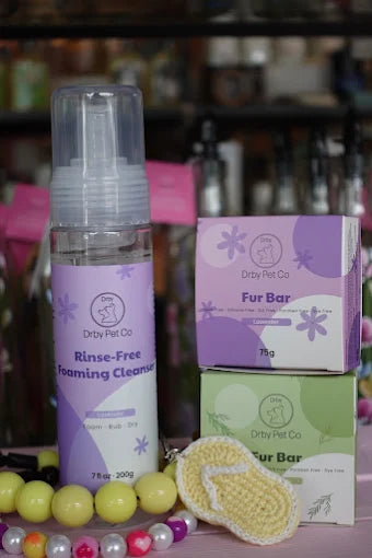 Dryly Pet Co pet care products including a bottle, box, and scrubber on a blurred background.