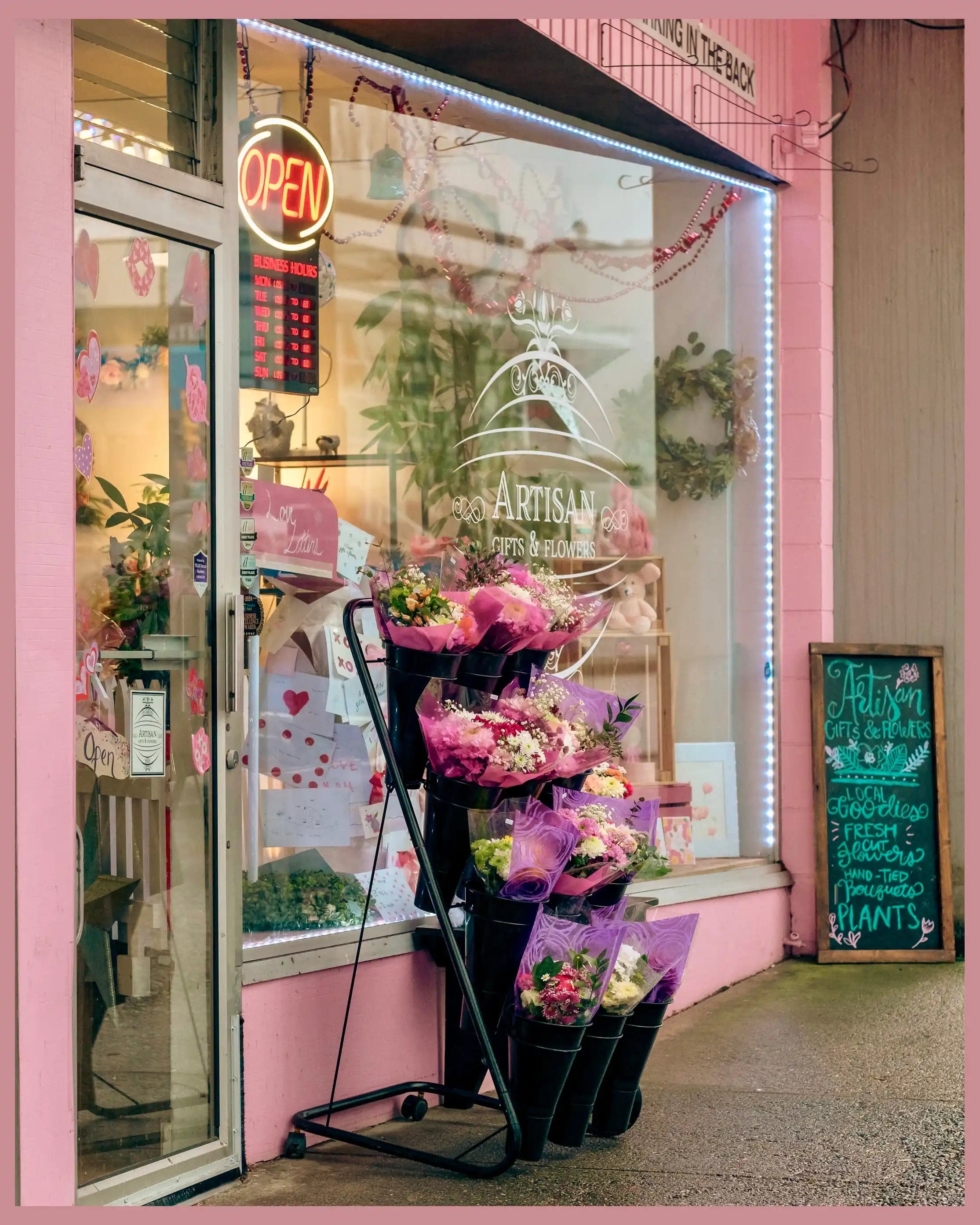 Pink flower shop with bouquets outside and 'Open' sign in window