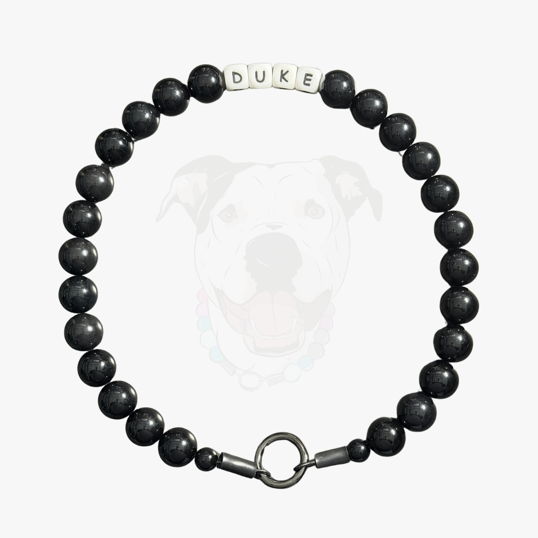Black beaded dog collar with 'DUKE' tag on a white background