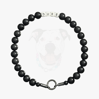 Black beaded dog collar with 'DUKE' tag on a white background