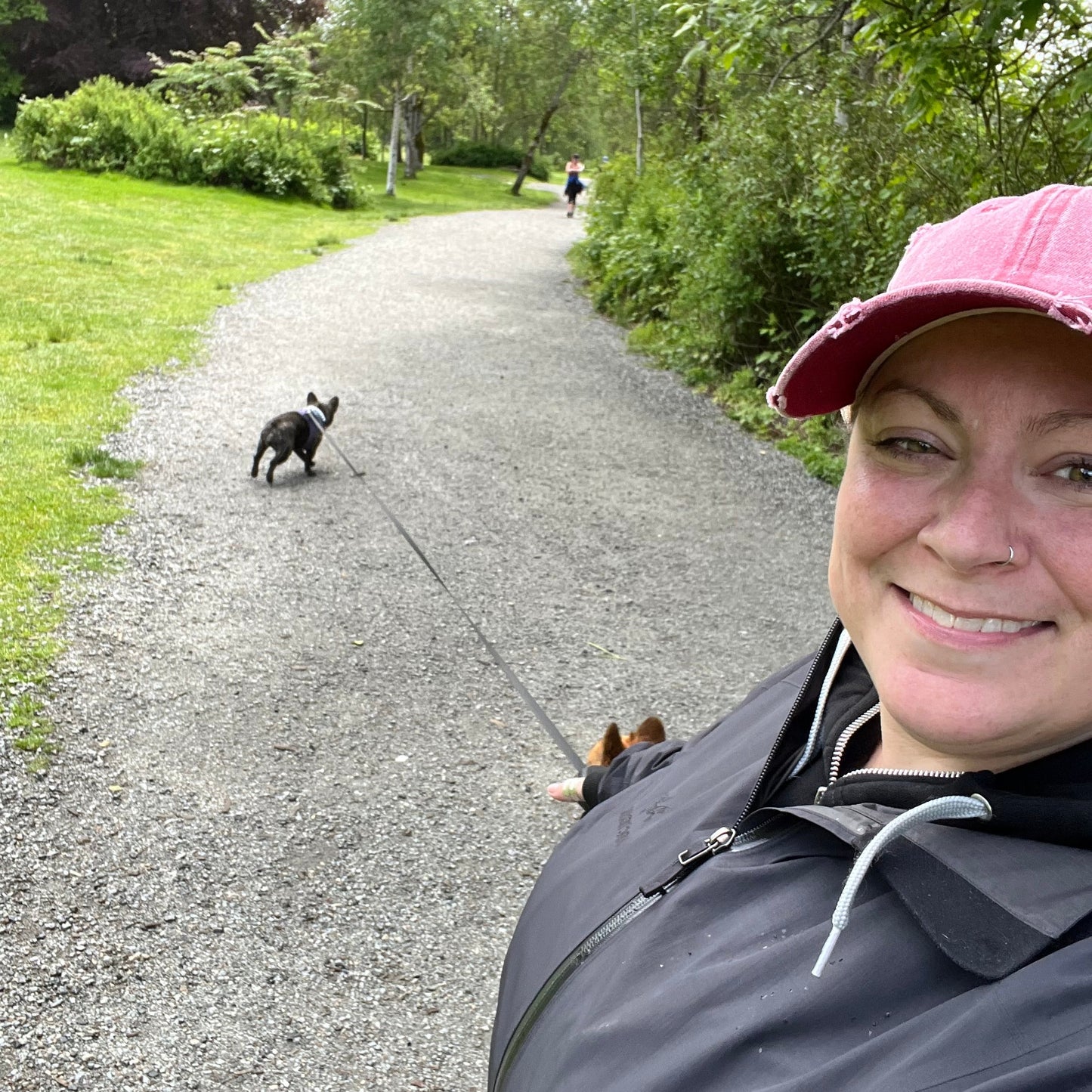 Person taking a selfie in a park with a dog on a leash in the background