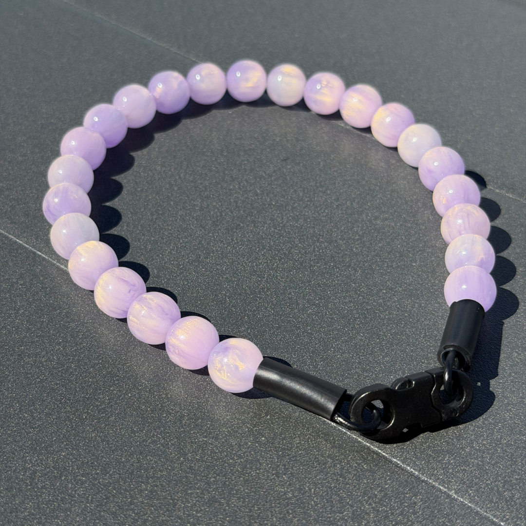 Purple beaded pet collar with a black clasp on a gray surface
