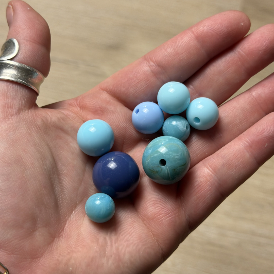 Hand holding blue and turquoise beads on a wooden surface