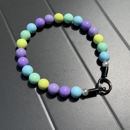 Julia beaded pet Collar crafted on aircraft grade stainless steel wire featuring pastel purple, yellow, blue and green acrylic solid beads. laying flat on a grey table