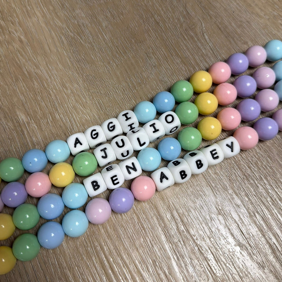 POPNCO Add On Alphabet Silicone Beads 12mm Colorful beaded bracelets with name beads on a wooden surface