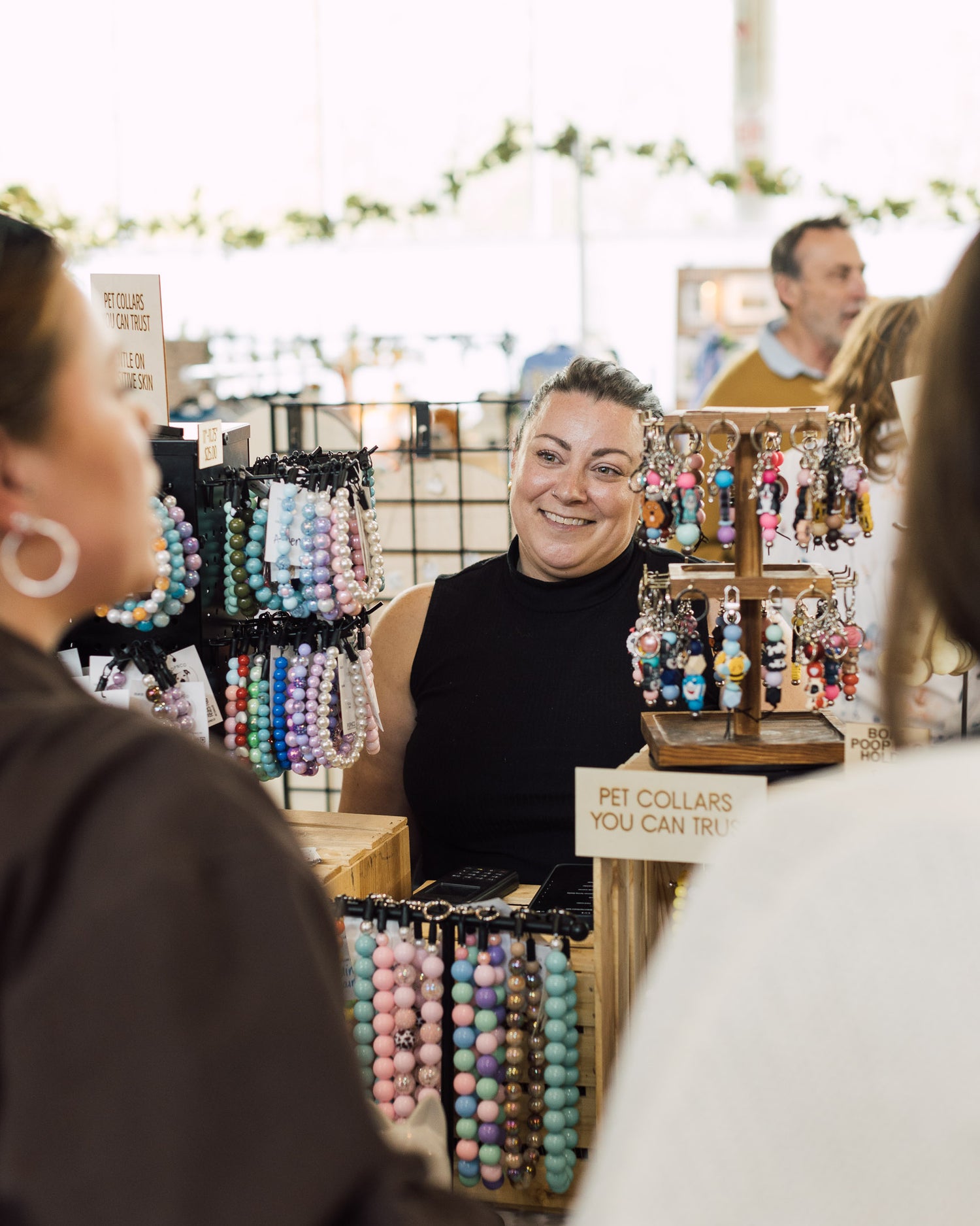 Founder Lisa Jeffery Standing behind her booth at a Market Event Smiling and talking with Customers about her company POPNCO Beaded pet Collars. 