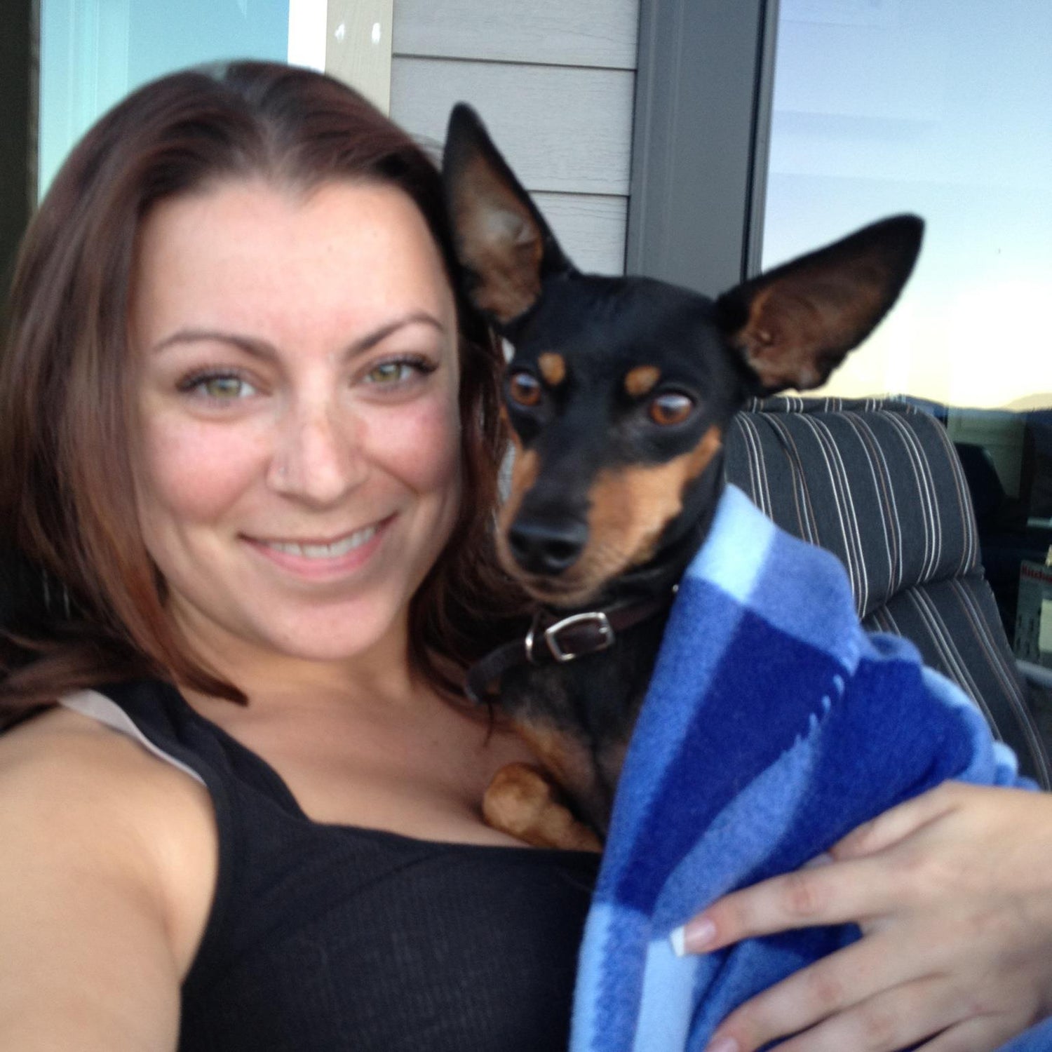 Woman holding a dog wrapped in a blue towel in front of some windows 