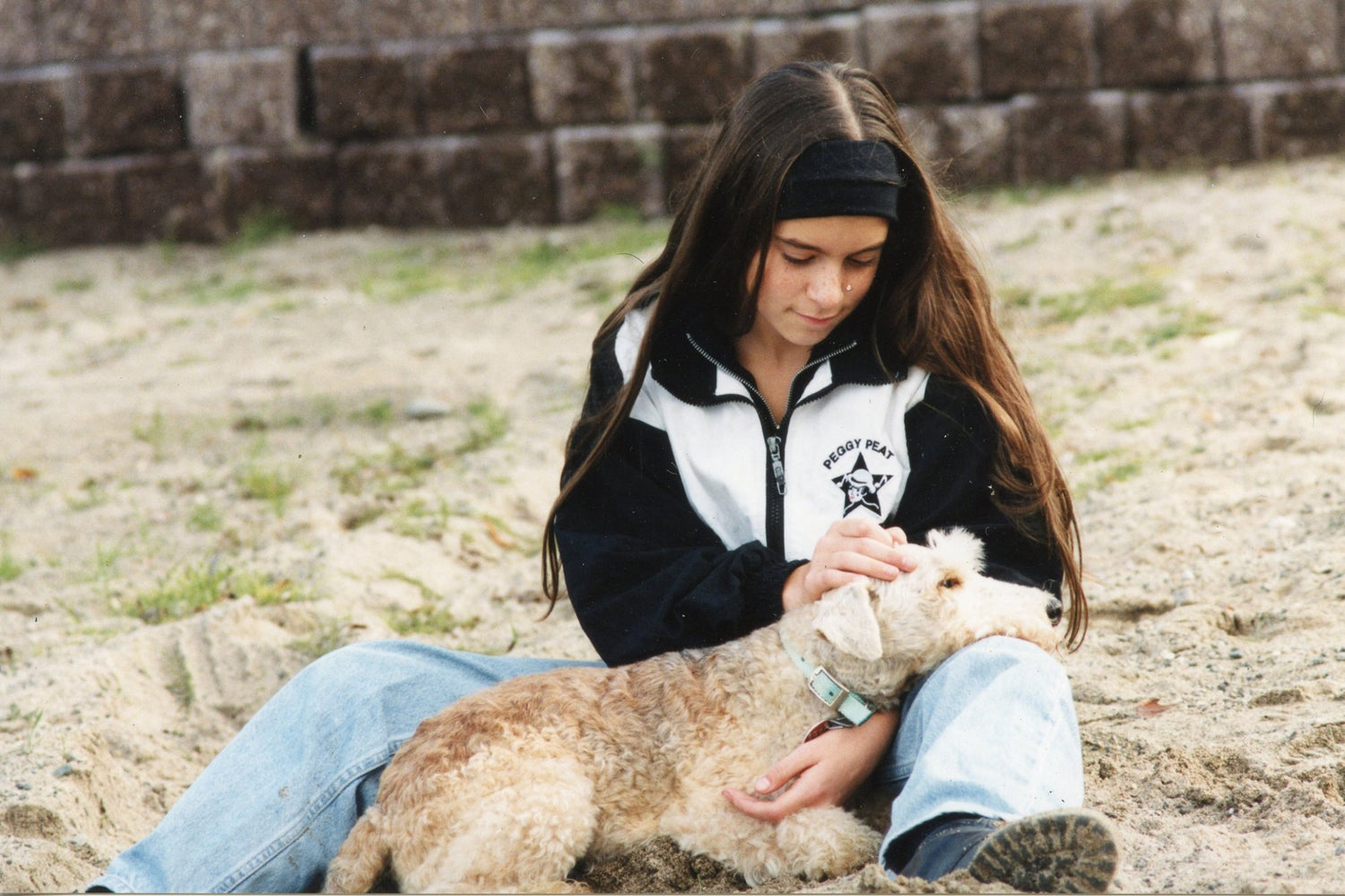 Person sitting on the ground with a dog, wearing a black and white jacket.