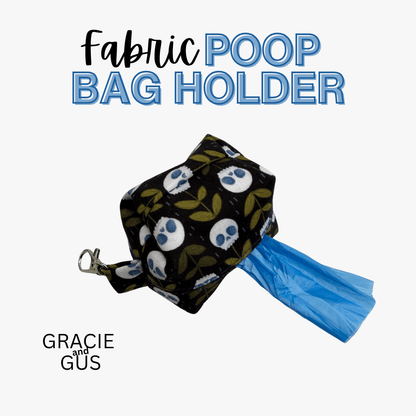 A fabric poop bag holder with a black background, white skulls, and olive green leaves, holding a blue plastic bag, shown on a light gray background with text reading 'Fabric POOP BAG HOLDER' and 'GRACIE and GUS'.
