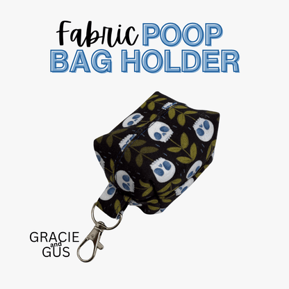 A fabric poop bag holder with a black background, white skulls, and green leaves, attached to a silver metal clasp. The text 'Fabric POOP BAG HOLDER' is displayed at the top, and 'GRACIE and GUS' is displayed at the bottom left on a light gray background.