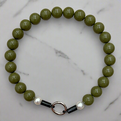 Green beaded bracelet with a black and silver clasp on a marble background