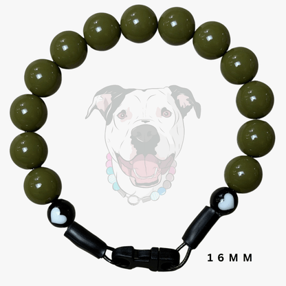 A beaded dog collar or bracelet made of glossy olive green round beads, with black adjustable slider clasp ends and a small white heart detail on one end. A faint dog face graphic appears behind the product, and '16 MM' text is shown at the bottom right.