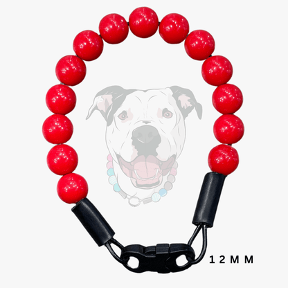 A red beaded dog collar with glossy round red beads, black plastic end caps, and a black quick-release clasp, shown on a light gray background with a faint dog illustration and '12 MM' text.