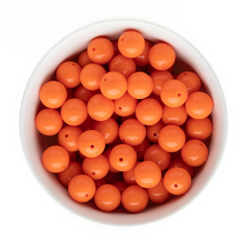 Bright orange round craft beads with pre-drilled holes, shown inside a white bowl from a top-down view on a white background.