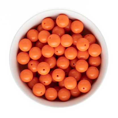 Bright orange round craft beads with pre-drilled holes, shown inside a white bowl from a top-down view on a white background.