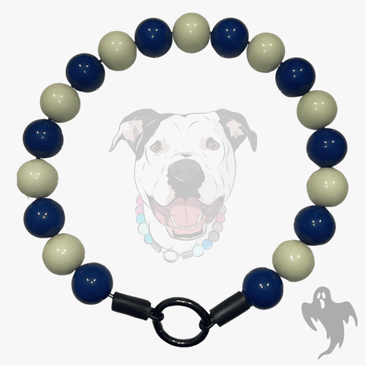 A beaded dog collar featuring alternating navy blue and cream-colored round beads, finished with a black toggle clasp and shown against a light gray background with a faint dog graphic.