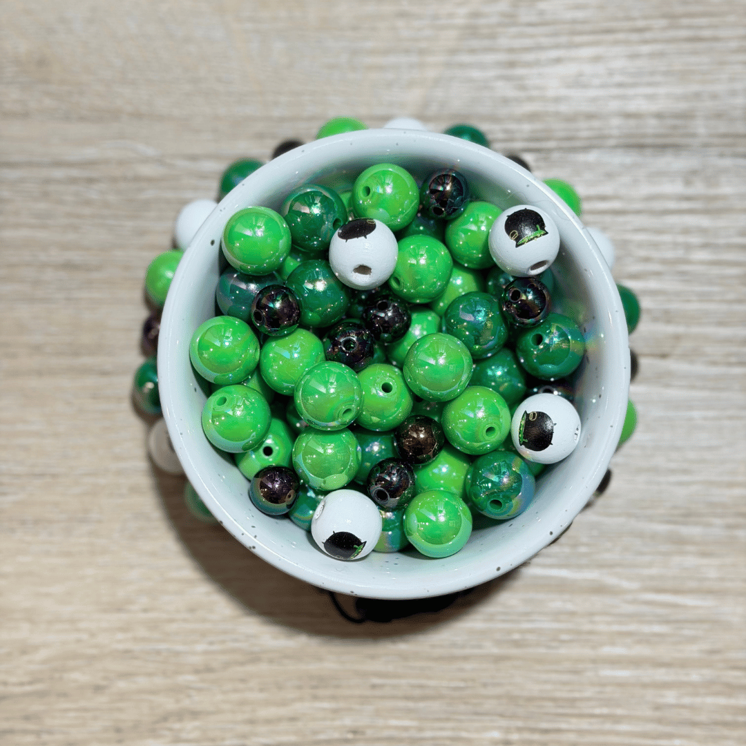 A top-down view of a white ceramic cup filled with green, black, and white marbled beads, set on a light wood surface.