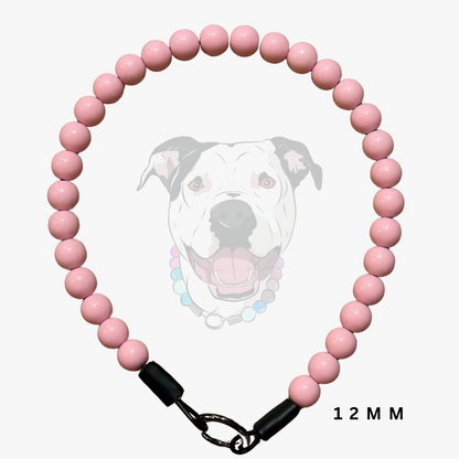 A pink beaded dog collar made of glossy round beads, featuring black plastic end caps and a silver metal clasp. A faint graphic of a dog's face is visible in the background, and the text '12 MM' is printed in the bottom right corner.