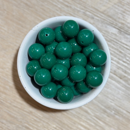 Green round beads with small holes, piled in a small white ceramic bowl on a light wood surface.