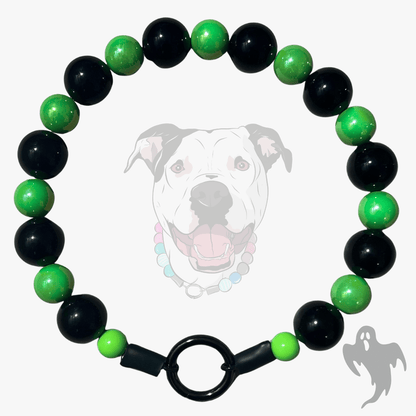 A beaded dog collar featuring alternating glossy black and vibrant green beads, finished with a black metal ring clasp. The product is displayed against a light gray background with a faint graphic of a pitbull dog wearing the collar and a small ghost shadow in the corner.