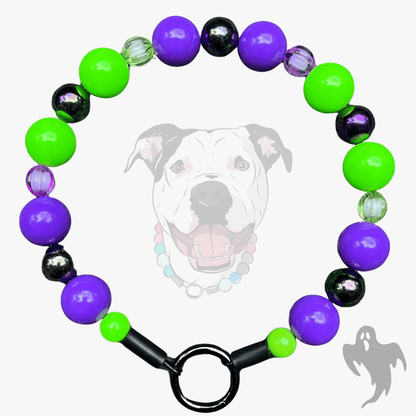 A beaded dog collar with purple, neon green, and black beads, featuring a black metal ring clasp. A faint graphic of a pitbull dog wearing the collar is displayed in the background.