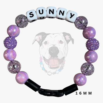 A pet collar bracelet featuring lavender and purple beads, some with glitter and some with a faceted crystal texture. It has white cube beads spelling out 'SUNNY' and a black plastic clasp.