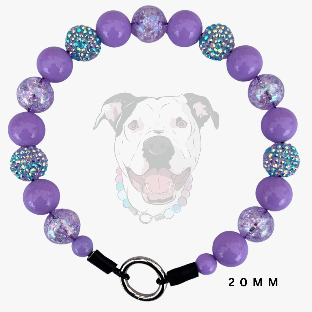 A purple beaded pet collar shown on a light gray background with a faded dog graphic behind it. The collar features smooth purple beads, faceted purple beads filled with glitter, and iridescent blue rhinestone-covered beads, finished with a black clasp and silver O-ring.