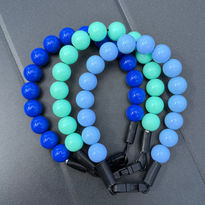 Dark Blue, Light Blue and Green beaded Pet collars from POPNCO Laying on a grey table. 