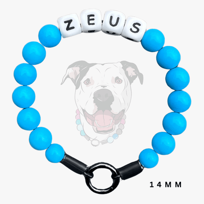 A beaded dog collar charm bracelet with bright blue round beads, a black toggle clasp, and white cube beads spelling 'ZEUS'. A faint dog illustration and the text '14 MM' appear on a light gray background.