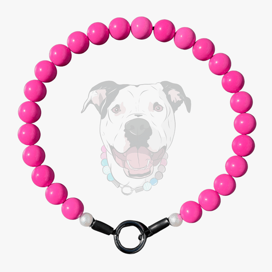 A beaded dog collar featuring bright pink round beads, white pearl-like end beads, and a black metal clasp, displayed against a light gray background with a faint graphic of a dog wearing the collar.