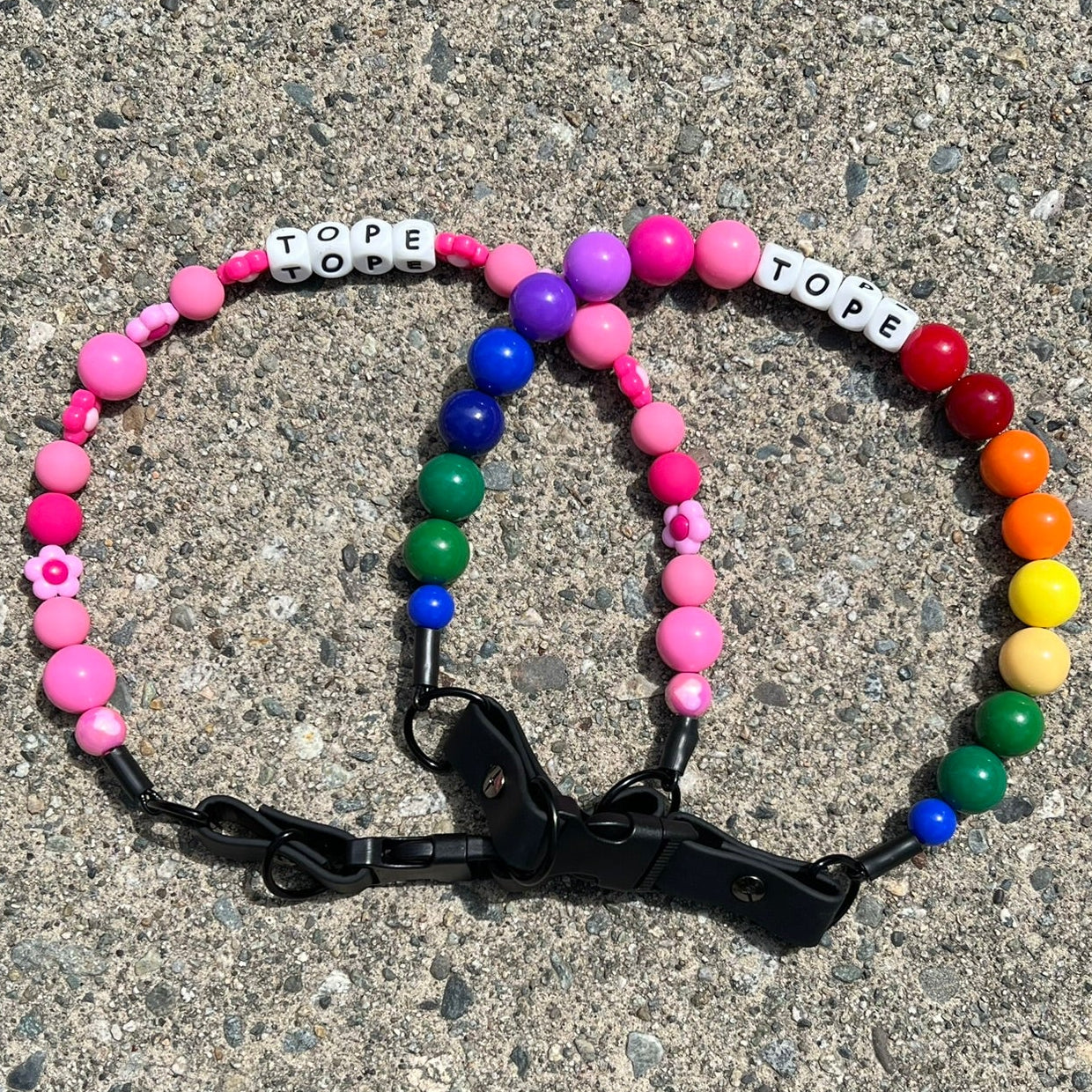 Colorful beaded POPNCO Pet Collars with letter beads on a concrete surface. They say TOPE, featuring Odessa pink and Rainbow in 20mm.