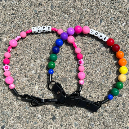 Colorful beaded POPNCO Pet Collars with letter beads on a concrete surface. They say TOPE, featuring Odessa pink and Rainbow in 20mm.